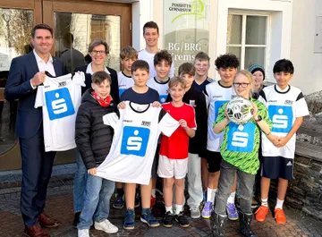Sechs Personen stehen um einen Stehtisch mit dem Logo des Österreichischen Roten Kreuzes, eine Person hält ein blaues Schild mit dem Sparkassen-Logo.