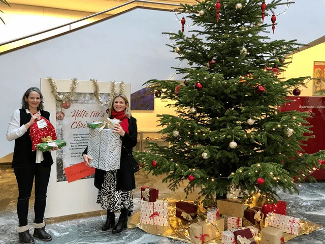 zwei Frauen mit Geschenk in der Hand neben dem Christbaum